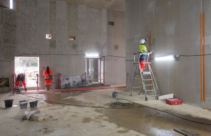 Les équipes réalisent les finitions des travaux de génie civil de la gare, ici polissage d’un mur.